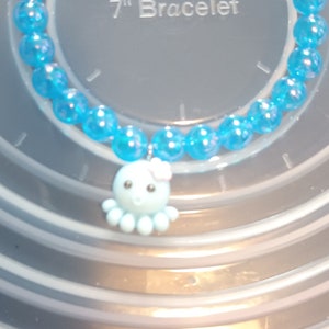 May include: A blue beaded bracelet with an octopus charm. The bracelet is approximately 17.78 cm in length. The charm is light blue with a pink bow.
