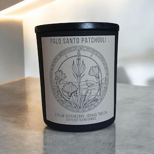 May include: Black candle jar with a white label that reads "Palo Santo Patchouli" and "Atrium Apothecary, Joshua Tree CA 200+6 Soy Blend Candle". The label also features a black and white illustration of a plant with flowers.