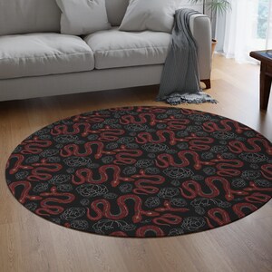 May include: A round black and red rug with a repeating pattern of white outlined red snakes and white flowers. The rug is on a wooden floor in a living room setting.