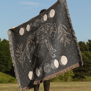 May include: A black woven tapestry with a gold wolf design and moon phases. The wolf is surrounded by stars and leaves.