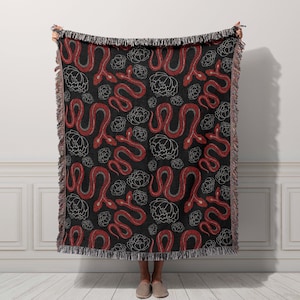 May include: A black woven throw blanket with a red snake and white flower pattern.