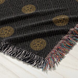 May include: Black and gold woven throw blanket with a geometric pattern and a pentagram design. The blanket has fringe on all sides.