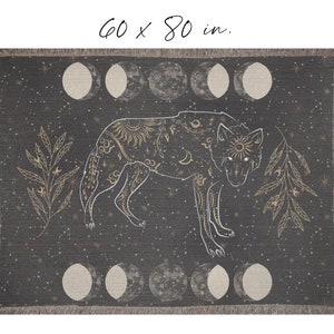 May include: A woven throw blanket with a dark gray background and a white wolf silhouette. The wolf is surrounded by gold stars, moons, and leaves. The blanket measures 60 x 80 inches.