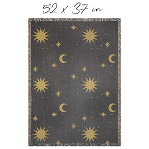 K&ouml;nnte beinhalten: Eine gewebte Wolldecke mit dunkelgrauem Hintergrund und einem Muster aus goldenen Sternen und Mondsicheln. Die Decke misst 132 x 94 cm.