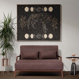 May include: A brown velvet loveseat with two pillows sits in front of a black and gold framed canvas print of a wolf with a moon and stars design. A small gold and black side table sits to the right of the loveseat.