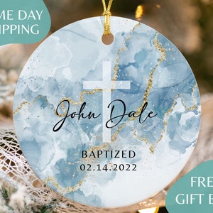 May include: A blue and gold round ornament with a white cross and the text "John Dale Baptized 02.14.2022".