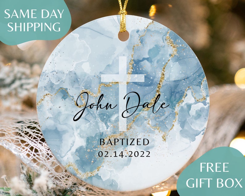 May include: A blue and gold round ornament with a white cross and the text "John Dale Baptized 02.14.2022".