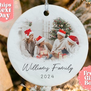 May include: White ceramic Christmas ornament with a photo of a family of four in front of a Christmas tree. The ornament has the text "Williams Family 2024" printed on it.
