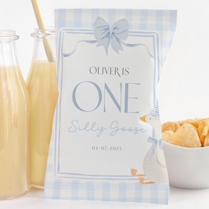 May include: A party favor bag with a blue and white gingham pattern, featuring the text "Oliver is One Silly Goose" and a cartoon goose illustration. The bag is filled with chips and is next to juice bottles with straws.