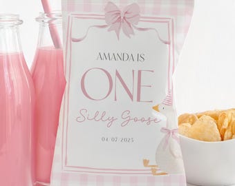 Może przedstawiać: Różowa i biała torba na przyjęcie z napisem "AMANDA IS ONE Silly Goose 04/07/2025" i ilustracją kreskówki gęsi. Dwie szklane butelki z różowym płynem z różowymi słomkami znajdują się po lewej stronie. Biała miska z chipsami znajduje się po prawej stronie.