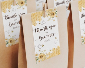 May include: Brown paper bags with yellow and white thank you tags that say "Thank you for bee-ing here!" The tags have a bee and honeycomb design with sunflowers.
