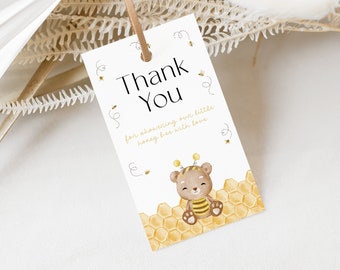 Puede incluir: Gracias por celebrar a nuestra pequeña abeja de miel con amor. Una tarjeta blanca con texto negro y una ilustración de dibujos animados de un oso marrón con un disfraz de abeja amarillo y negro sentado en un panal.