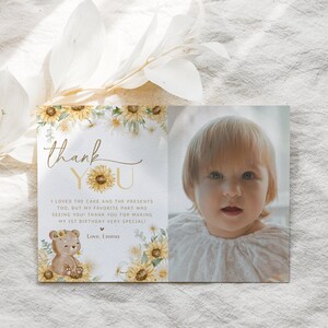 May include: A thank you card with a sunflower and daisy floral design. The card features a photo of a young child and the text "thank you" with a sunflower graphic. The text reads "I loved the cake and the presents too, but my favorite part was seeing you! Thank you for making my 1st birthday very special! Love, Emma."