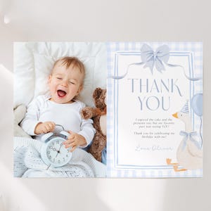 May include: A baby boy smiles while holding a light blue alarm clock, next to a teddy bear. A thank you card features a blue gingham pattern, a goose illustration, and the words "THANK YOU".