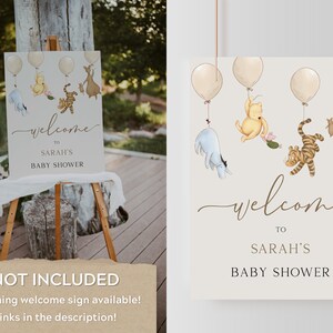 May include: A welcome sign for a baby shower with a Winnie the Pooh theme. The sign features Winnie the Pooh, Piglet, Tigger, and Eeyore characters with balloons. The text on the sign reads "Welcome to Sarah's Baby Shower".