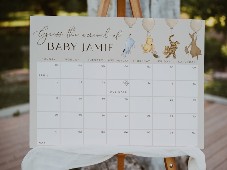 May include: A white calendar with a Winnie the Pooh theme for a baby shower. The calendar has the months of April and May with the days of the week listed. The due date is marked with a heart on April 13th. The text "Guess the arrival of Baby Jamie" is at the top of the calendar.