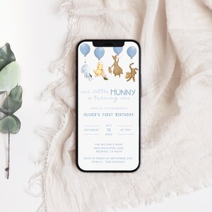 May include: A blue and white smartphone screen displaying a Winnie the Pooh themed first birthday invitation for a baby named Oliver. The invitation features Winnie the Pooh and his friends Piglet, Tigger, and Eeyore holding blue balloons. The text on the invitation reads "our little HUNNY is turning one" and includes the date, time, and location of the party.