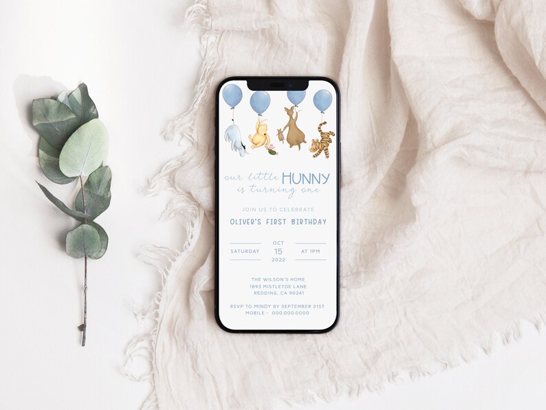 May include: A blue and white smartphone screen displaying a Winnie the Pooh themed first birthday invitation for a baby named Oliver. The invitation features Winnie the Pooh and his friends Piglet, Tigger, and Eeyore holding blue balloons. The text on the invitation reads "our little HUNNY is turning one" and includes the date, time, and location of the party.