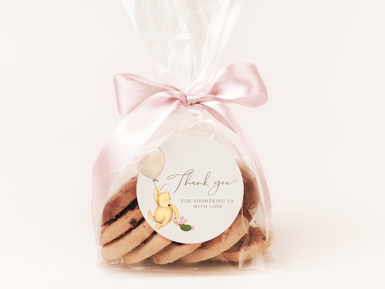 May include: A clear plastic bag filled with cookies tied with a pink ribbon. A round sticker with a cartoon Winnie the Pooh character holding a balloon and the text "Thank you for showering us with love" is attached to the bag.
