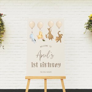 K&ouml;nnte beinhalten: Ein Winnie Puuh-Motto-Schild f&uuml;r eine 1. Geburtstagsparty mit Ballons, Winnie Puuh, Ferkel, Esel und Tiger. Das Schild lautet "Willkommen zu Aprils 1. Geburtstag 10/05/2023".