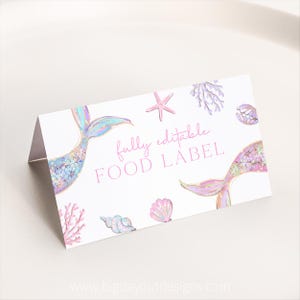 Peut inclure: Étiquette alimentaire pliée blanche avec des illustrations de queues de sirène dans des tons de rose, bleu et violet. L'étiquette est ornée d'étoiles de mer, de coquillages et de coraux. Le texte "fully editable FOOD LABEL" est imprimé en rose.