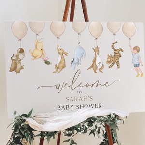 Peut inclure: Une pancarte de bienvenue pour la f&ecirc;te pr&eacute;natale de Sarah avec Winnie l'ourson et ses amis tenant des ballons. La pancarte est blanche avec du texte et des illustrations marrons.