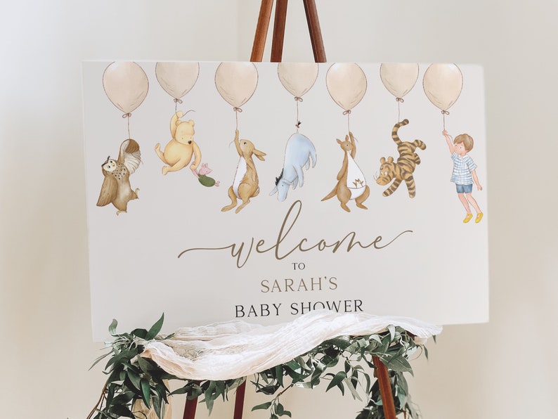 Peut inclure: Une pancarte de bienvenue pour la f&ecirc;te pr&eacute;natale de Sarah avec Winnie l'ourson et ses amis tenant des ballons. La pancarte est blanche avec du texte et des illustrations marrons.
