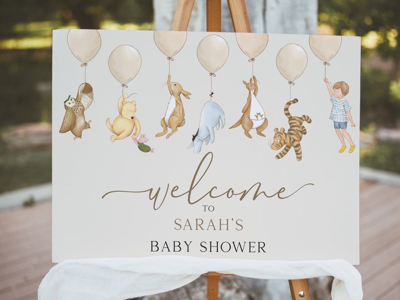 Peut inclure: Une pancarte de bienvenue pour une f&ecirc;te pr&eacute;natale sur le th&egrave;me de Winnie l'ourson avec un fond brun clair. La pancarte pr&eacute;sente une cha&icirc;ne de ballons avec Winnie l'ourson et ses amis qui pendent. Le texte sur la pancarte indique "Bienvenue &agrave; la f&ecirc;te pr&eacute;natale de Sarah".