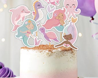 May include: A pink and white frosted cake decorated with mermaid themed cake toppers. The toppers include a mermaid, a seahorse, a dolphin, a turtle, an octopus, and a fish.