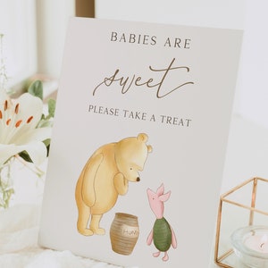 May include: A Winnie the Pooh themed baby shower sign with a yellow bear and a pig holding a pot of honey. The sign reads "Babies are sweet. Please take a treat."