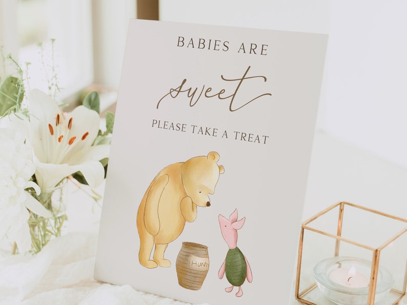 May include: A Winnie the Pooh themed baby shower sign with a yellow bear and a pig holding a pot of honey. The sign reads "Babies are sweet. Please take a treat."