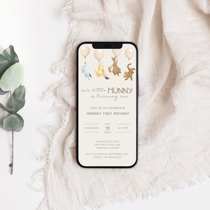 May include: A Winnie the Pooh themed first birthday invitation on a smartphone screen. The invitation features a cartoon illustration of Winnie the Pooh, Piglet, Tigger, and Eeyore holding balloons. The text on the invitation reads "our little HUNNY is turning one" and includes details for the birthday party, including the date, time, and location.