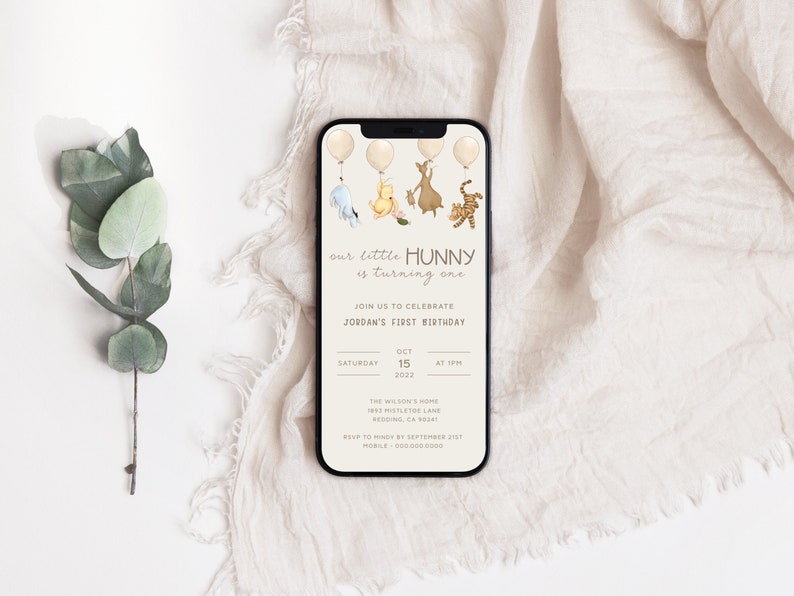 May include: A Winnie the Pooh themed first birthday invitation on a smartphone screen. The invitation features a cartoon illustration of Winnie the Pooh, Piglet, Tigger, and Eeyore holding balloons. The text on the invitation reads "our little HUNNY is turning one" and includes details for the birthday party, including the date, time, and location.