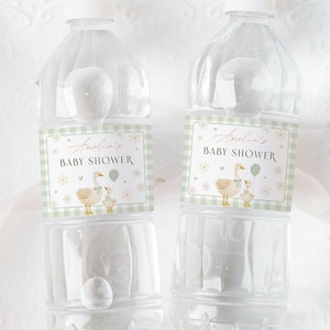 May include: Two clear plastic water bottles with labels for a baby shower. The labels feature a green gingham border, the text "Amelia's BABY SHOWER", and an illustration of a mother duck and duckling with a balloon.