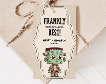Op de afbeelding: Een Halloween-cadeaulabel met een cartoonillustratie van Frankenstein's monster. De tekst luidt: "Frankly I think you are the BEST! Happy Halloween! From Jake." Het label is met touw aan een beige geschenkdoos bevestigd.