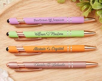 May include: Four personalized pens with rose gold accents. The pens are in different colors: pink, green, orange, and rose gold. The pens are engraved with names and symbols, such as hearts and stars.