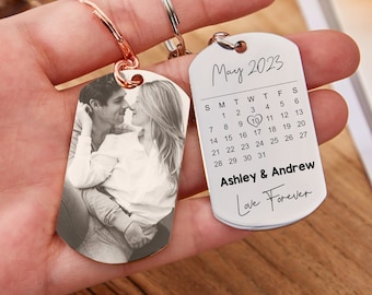 May include: A silver keychain with two tags. One tag has a black and white photo of a couple. The other tag has a calendar for May 2023 with the date 10 circled and the text "Ashley & Andrew Love Forever".