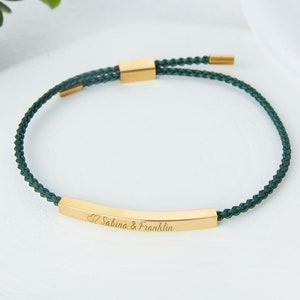 Puede incluir: Un brazalete de cordón verde con una barra dorada que tiene la inscripción "Sabina & Franklin" con dos corazones.