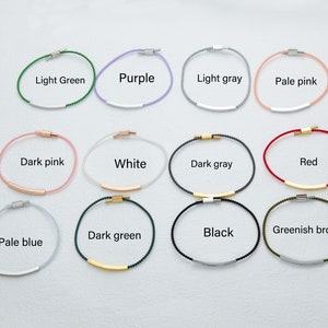 May include: A collection of minimalist bracelets in various colors, including light green, purple, light gray, and pale pink. Each bracelet features a thin cord with a metallic bar and clasp. The text labels each color.