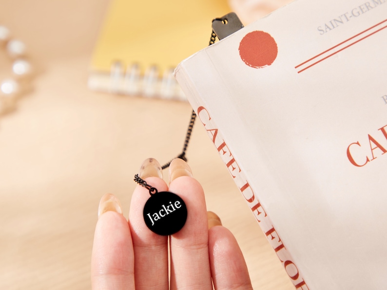 May include: A black necklace with a round pendant that says "Jackie" in white lettering.