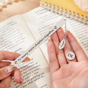 May include: Silver bookmark with a feather charm and a round charm with the initials "DK" engraved. The bookmark has the text "To many more chapters together" engraved on it.