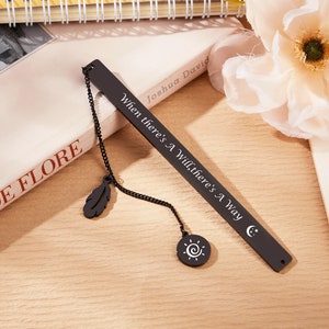 May include: Black metal bookmark with a chain and two charms, a feather and a sun. The bookmark is engraved with the quote "When there's a will, there's a way."