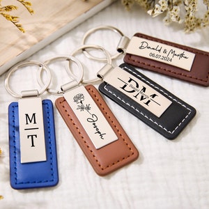 May include: Four personalised leather keyrings with metal rings. One keyring is blue with the initials "M" and "T". Another keyring is brown with a flower design and the name "Joseph". A third keyring is black with the initials "DM" and the name "Daniel Morris". The final keyring is brown with the text "Donald & Martha 06.07.2024".