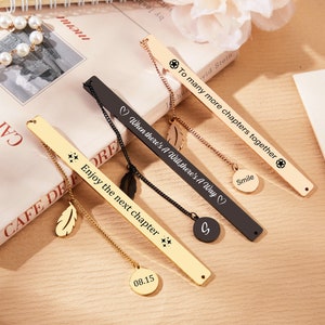 May include: Set of five gold and black metal bookmarks with different inspirational quotes and charms. The bookmarks feature a feather charm, a star charm, a heart charm, and a circle charm. The quotes include "To many more chapters together", "When there's a will, there's a way", "Enjoy the next chapter", and "Smile".