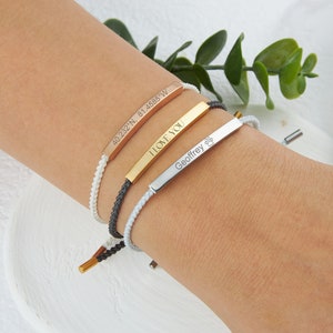 May include: Three personalized bar bracelets in rose gold, gold, and silver. The rose gold bracelet has coordinates, the gold one says "I LOVE YOU", and the silver one has a paw print and the name "Geoffrey". Each bracelet has a braided cord.