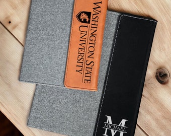May include: Two gray and black fabric laptop sleeves. The top sleeve has a brown leather flap with the text "WASHINGTON STATE UNIVERSITY" and a logo. The bottom sleeve has a white monogram with the text "MICHAEL" on the front.