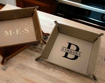 May include: Two brown leather valet trays with personalized monograms. One tray has the initials "M.E.S." and the other has the initial "B" with the name "BARBARA" underneath.