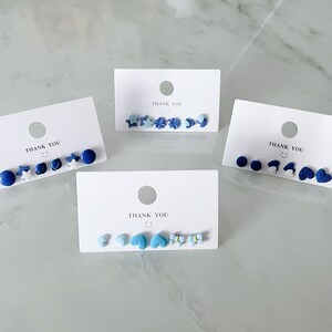 May include: Four cards with the text "Thank You" printed on them. Each card has a set of blue and white stud earrings with different shapes, including stars, hearts, and circles.