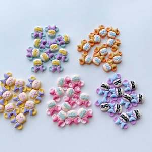 May include: Assortment of colorful resin bear charms with bows and eye patches. The charms are in shades of pink, purple, yellow, and orange.