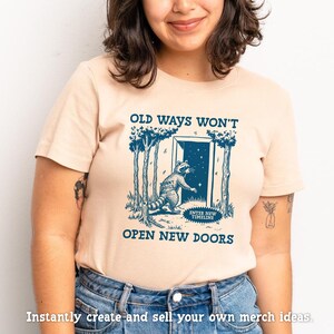 May include: A light beige t-shirt with a blue graphic of a raccoon opening a door with the text "Old ways won't open new doors".